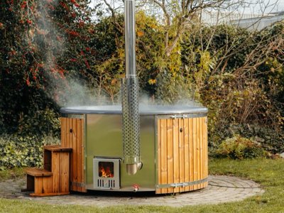 De Comfort hottub met Thermowood ombouw, RVS kachel en trap, dampend in een tuin